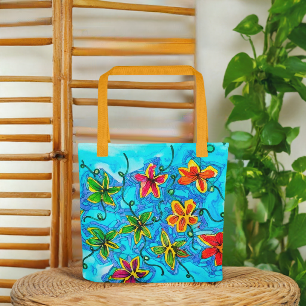 Flower Patch Tote bag with colorful floral artwork by Joy Calonico and yellow handles on a woven surface